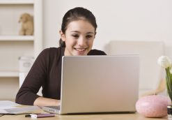 A young girl is working on a laptop, smiling, and looking away from the camera. Horizontally framed shot.